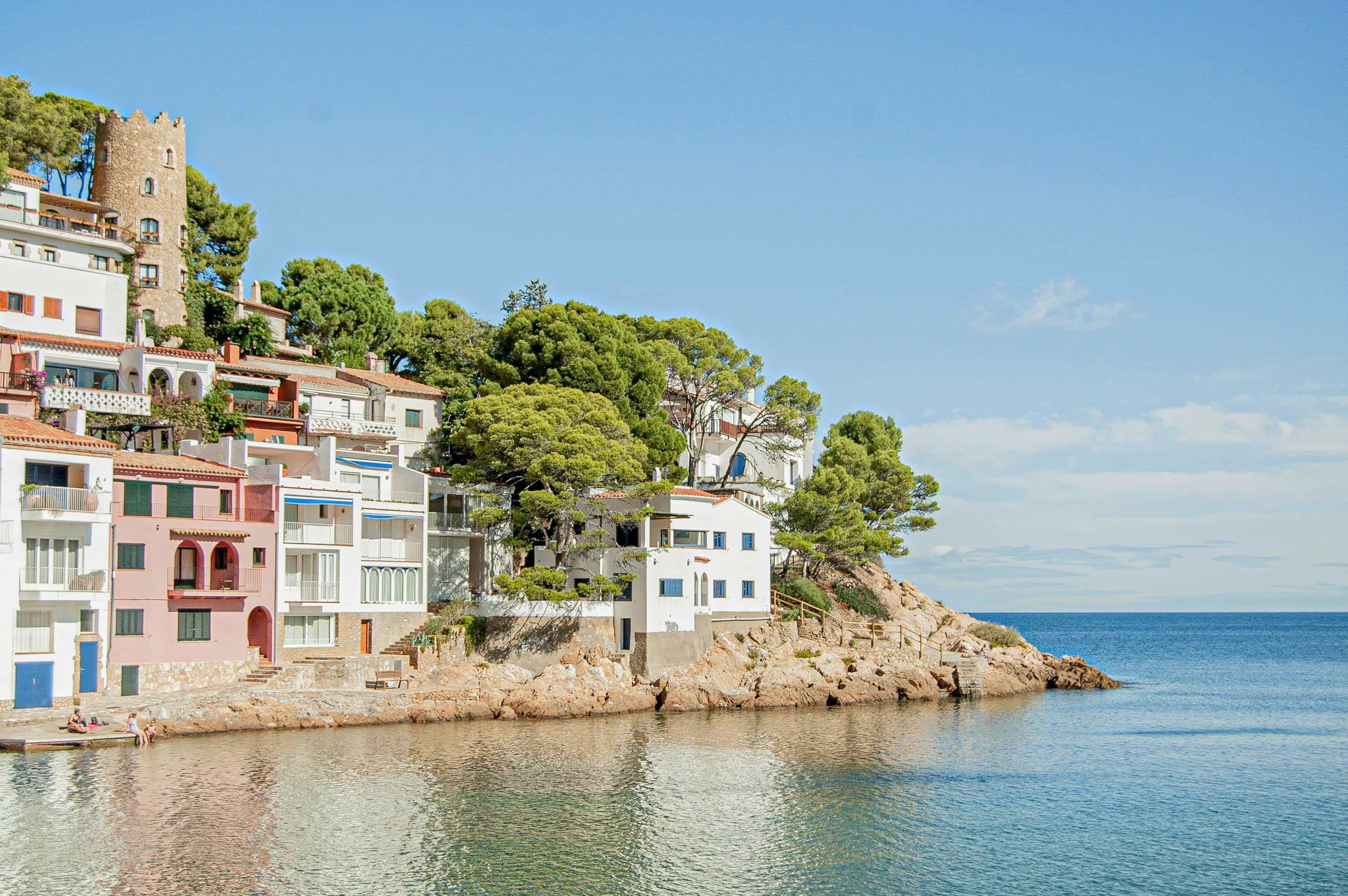 La cala de Sa Tuna, en Begur: casas blancas y rosadas de pescador junto al agua, con una torre de piedra sobre el promontorio y pinos