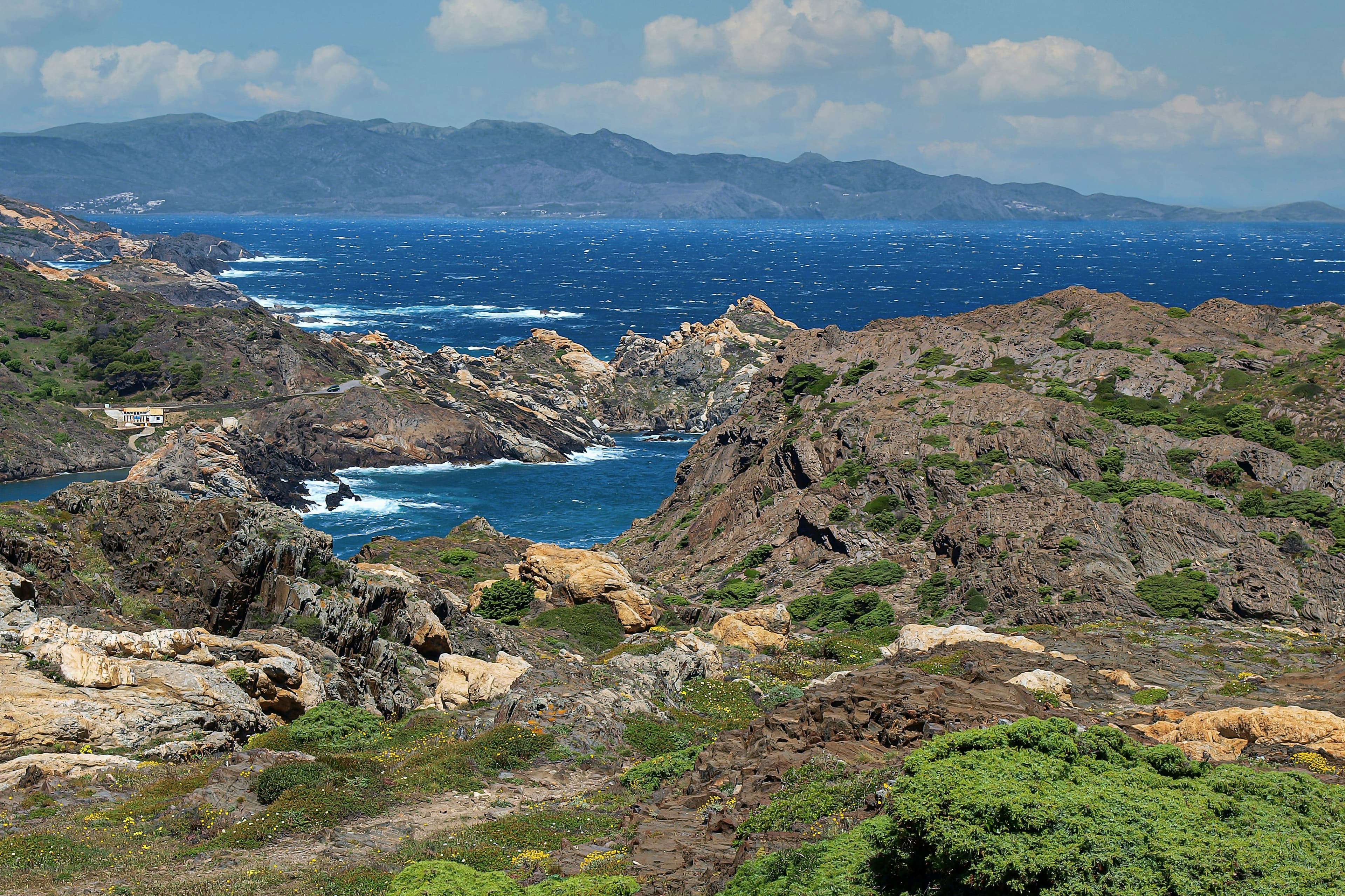 El paisaje de roca esculpida del Cap de Creus cayendo al mar azul, con la sierra al fondo