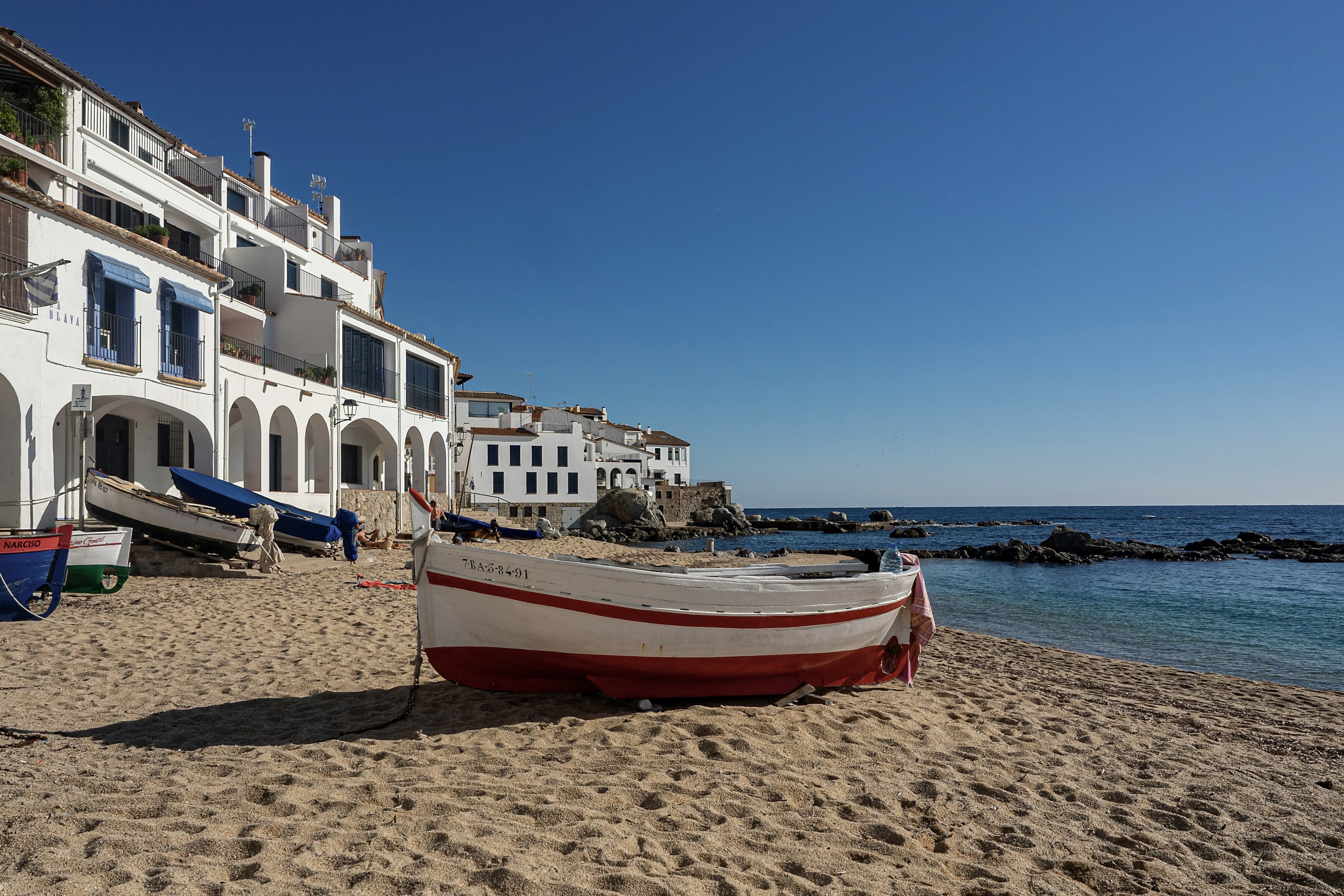Las voltes blancas de Port Bo abiertas sobre la playa de Calella de Palafrugell, con una barca de pesca varada en la arena