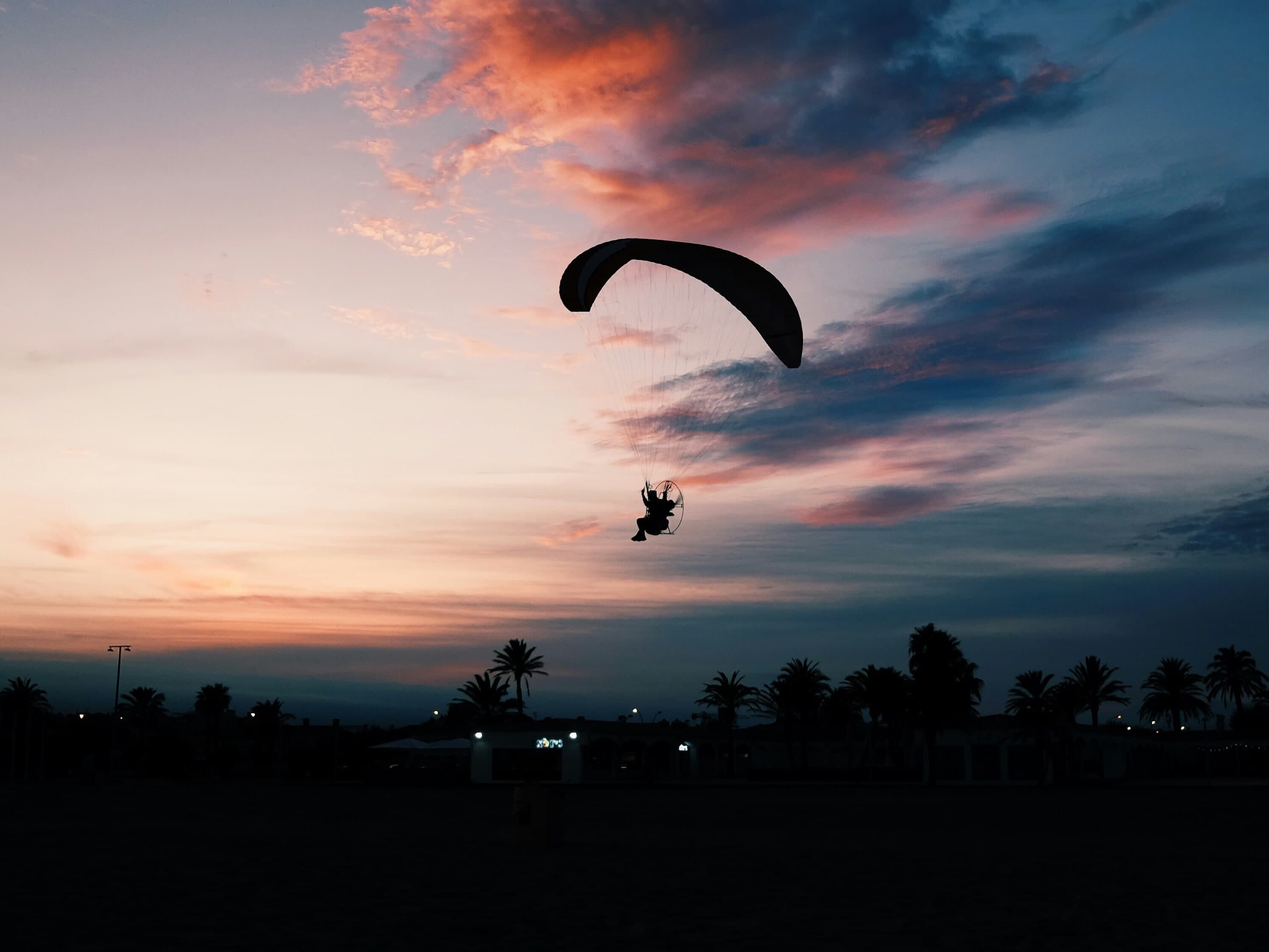 Un paramotor sobrevuela la playa de Empuriabrava recortado contra un cielo de nubes rosadas al atardecer