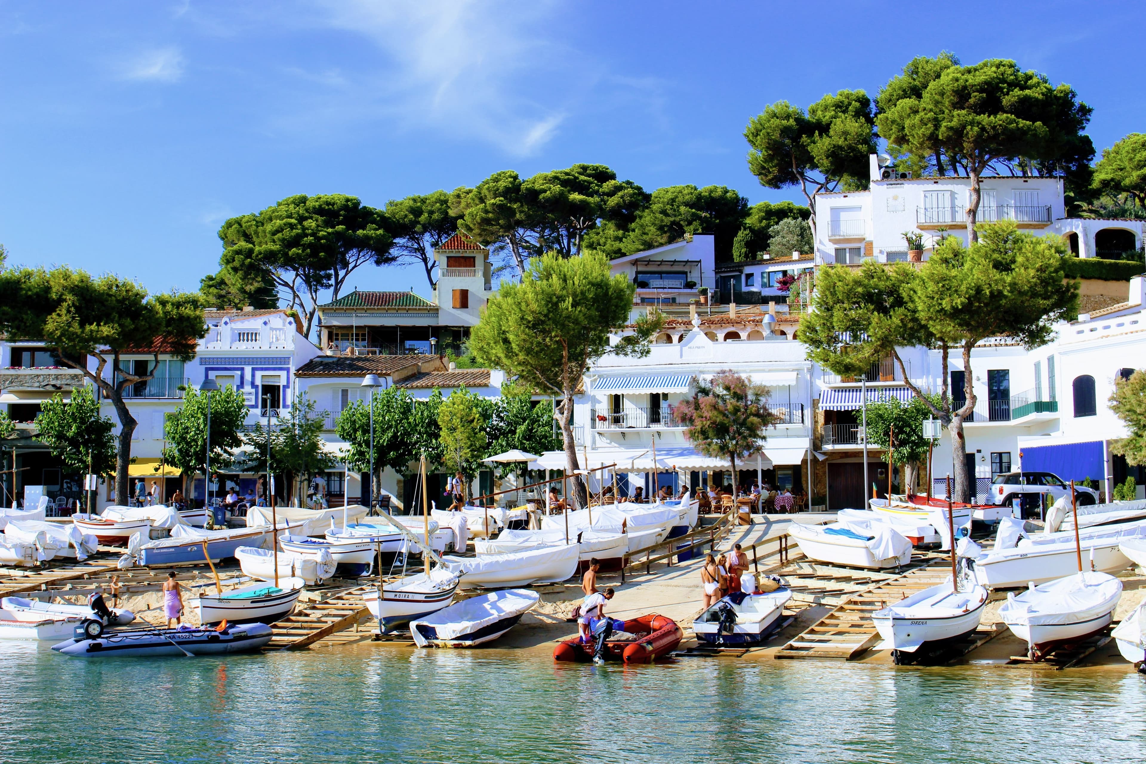 El paseo marítimo de Llafranc con las barcas de madera varadas en la arena y las casas blancas entre pinos