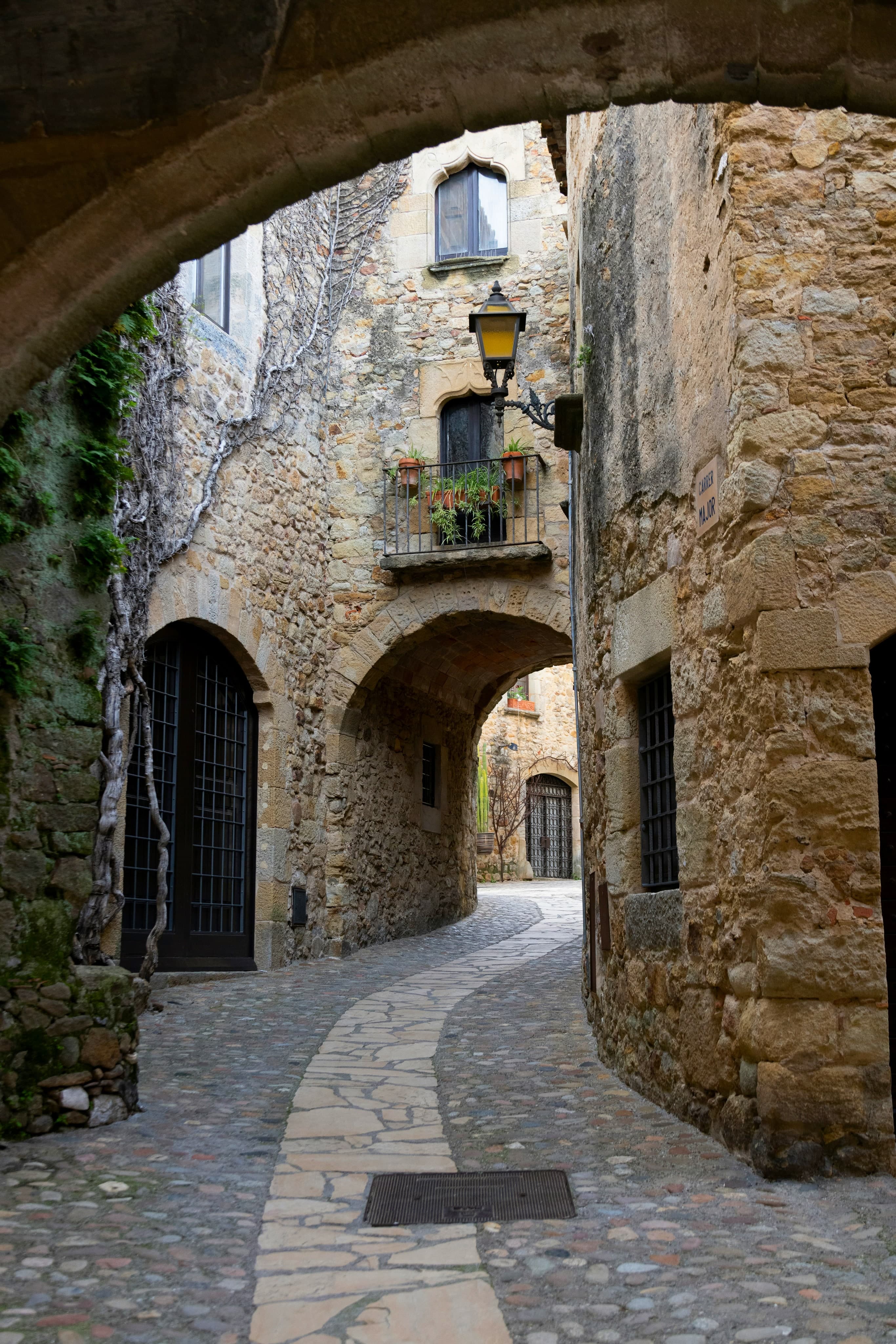 Una calle empedrada del recinto gótico de Pals, con casas de piedra dorada, arcos y una farola de forja