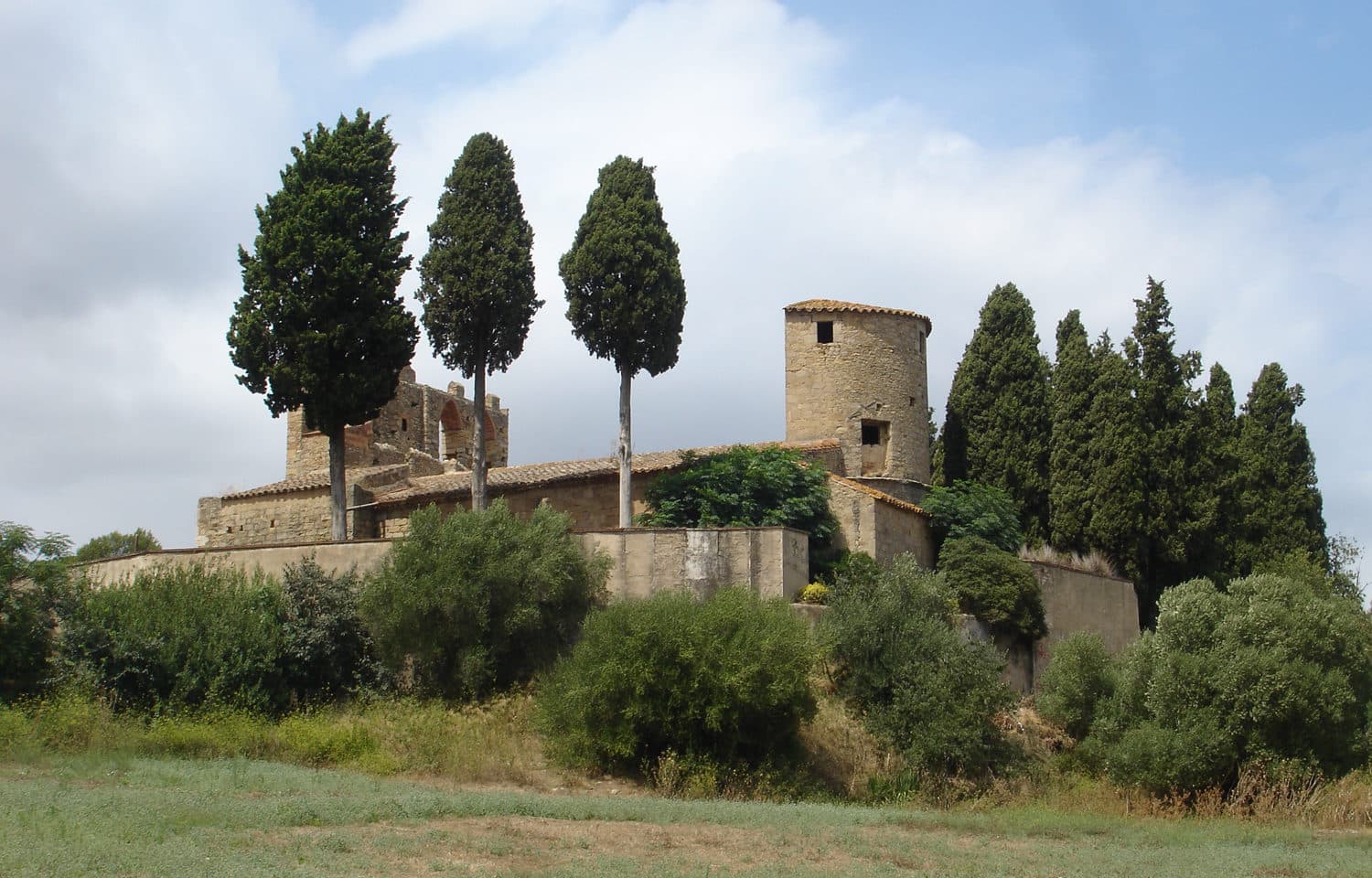La iglesia románica de Sant Esteve de Peratallada, con su torre y tres cipreses, sobre la llanura del Empordà