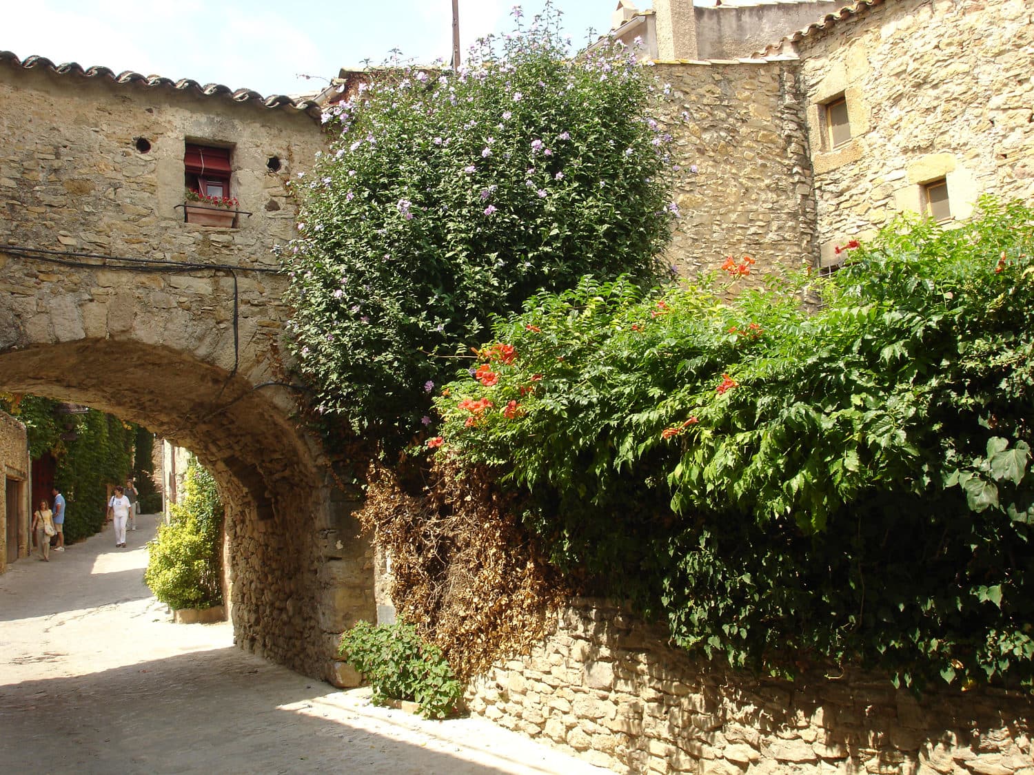 Un arco de piedra en la entrada de una calle de Peratallada, con buganvillas y otras flores trepando por el muro