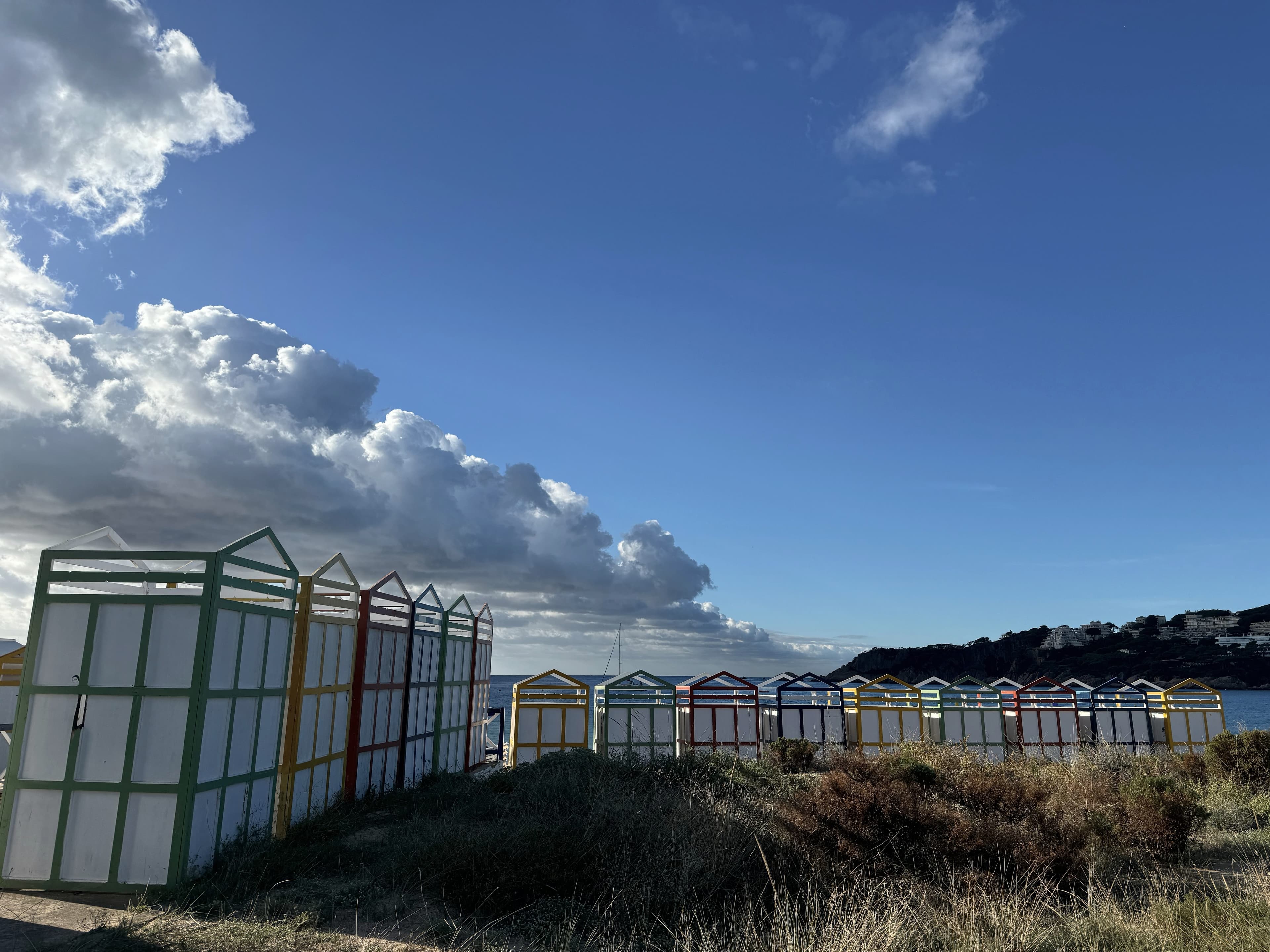 La fila de casetas de madera de colores de S’Agaró alineadas sobre la duna de la Platja de Sant Pol, con el mar y el cabo al fondo