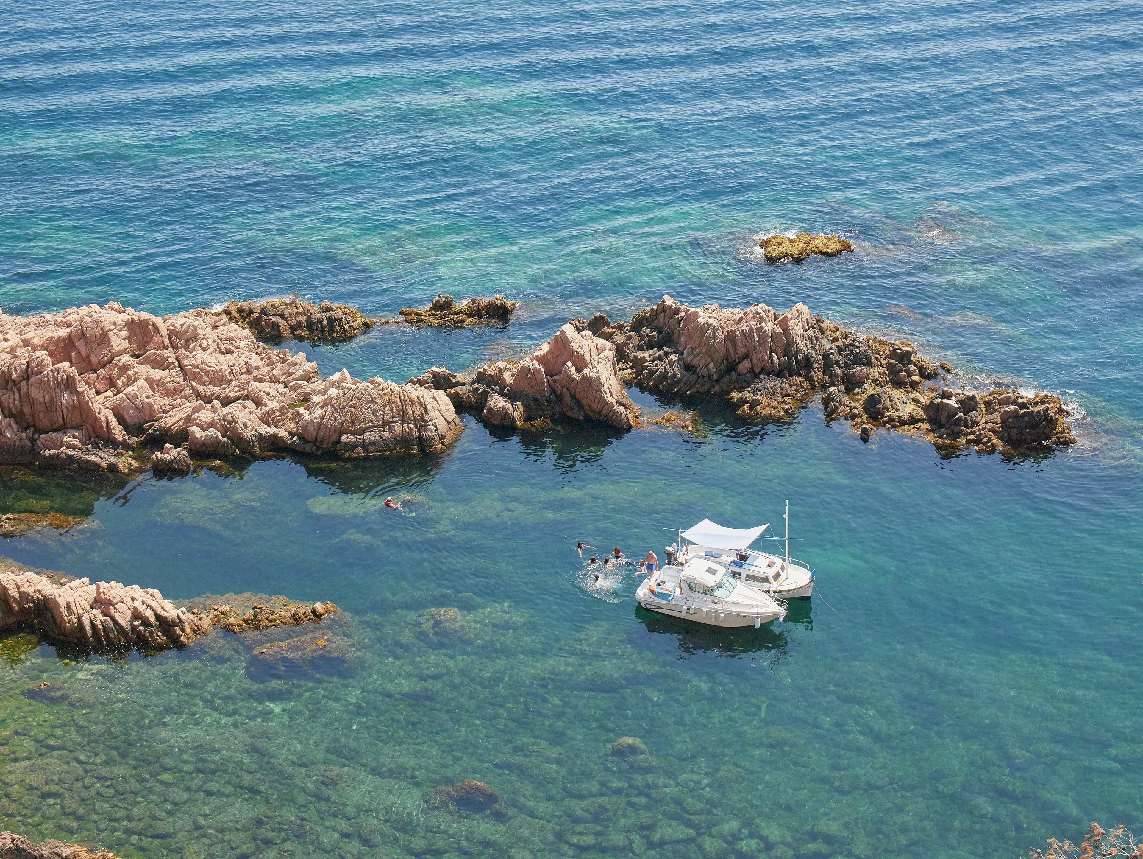 Una cala rocosa de agua turquesa cerca de Sant Feliu de Guíxols, con roca rojiza y una barca fondeada