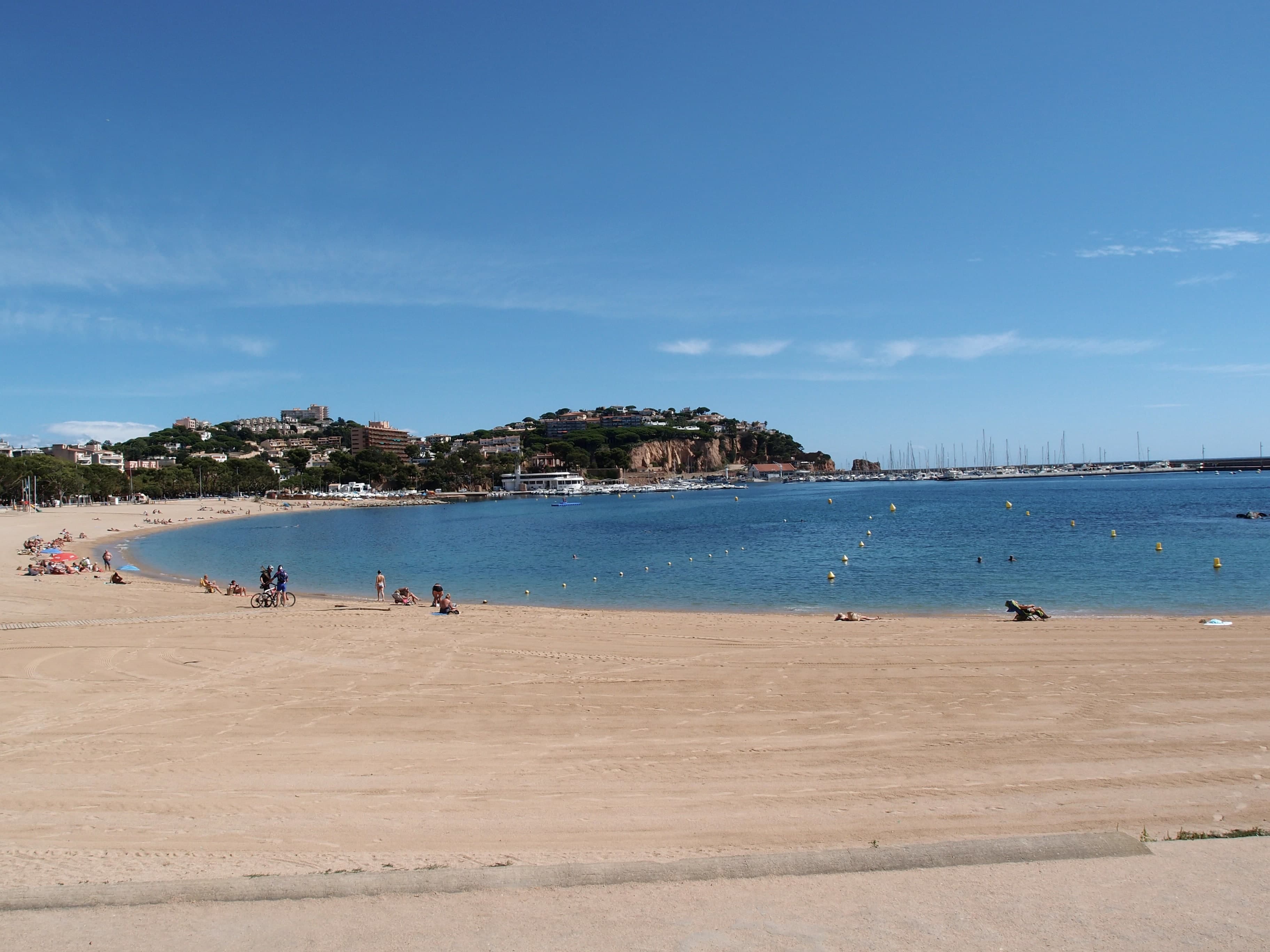 La amplia playa de Sant Feliu de Guíxols y su bahía, con el puerto deportivo y el cabo al fondo