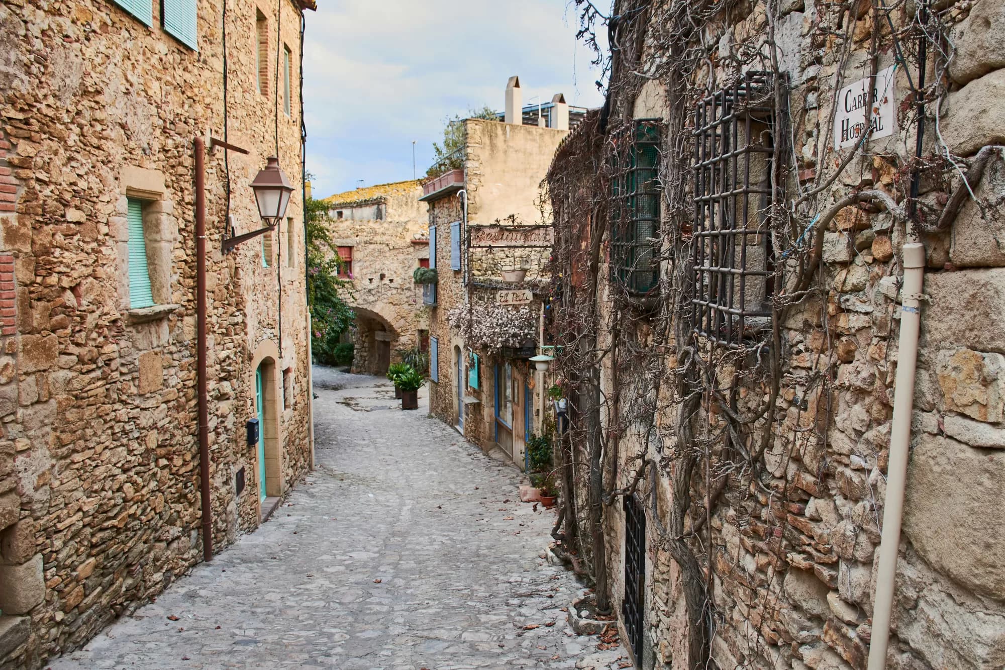 Callejón empedrado bajo un arco de piedra en Peratallada, con buganvillas en flor