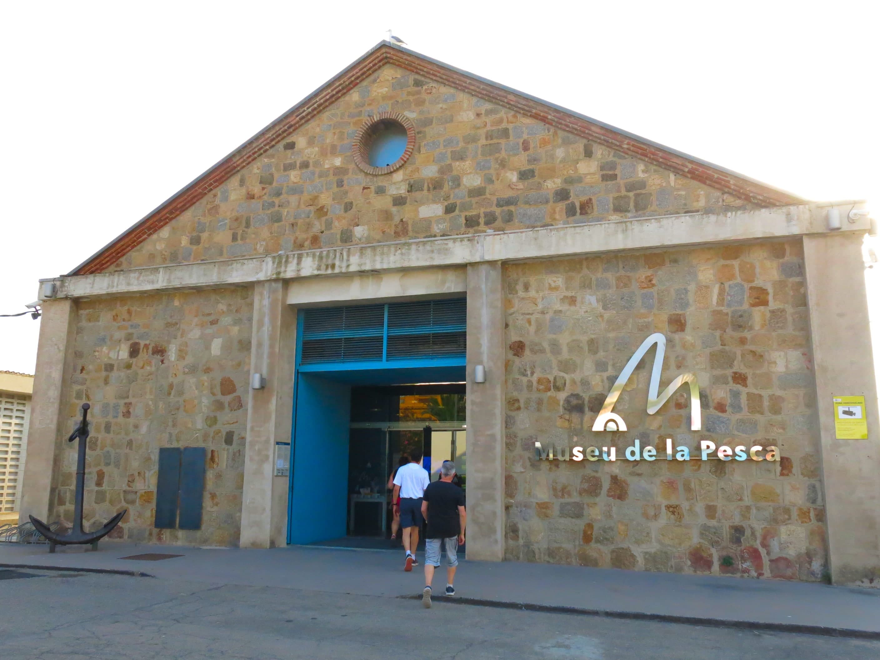 Fachada de piedra del Museu de la Pesca en el puerto de Palamós, con un ancla junto a la entrada