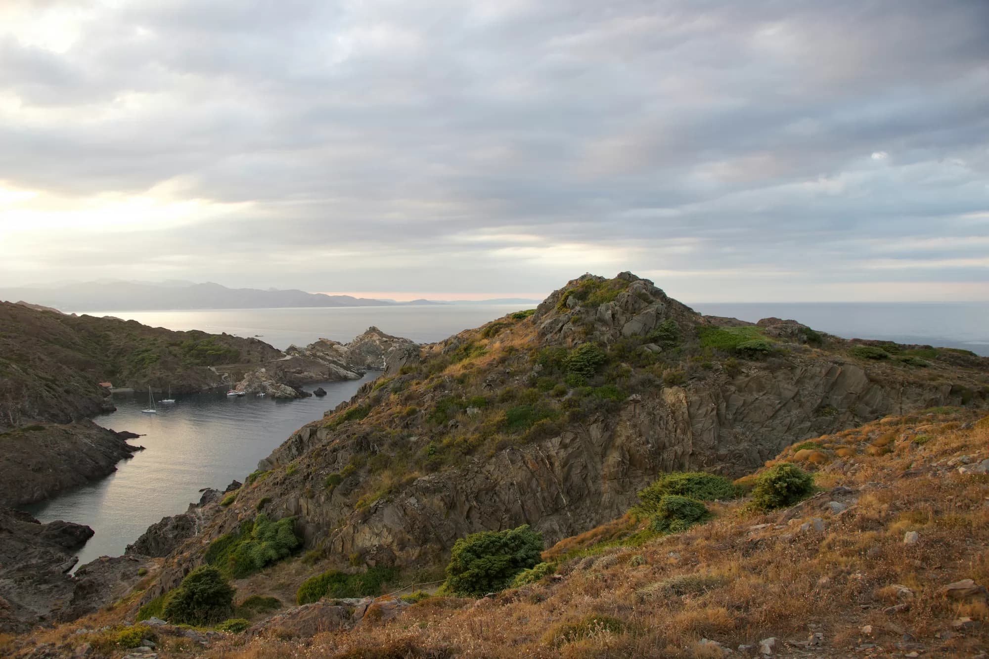 El paisaje rocoso del Cap de Creus visto desde lo alto, con una cala y barcas fondeadas al fondo