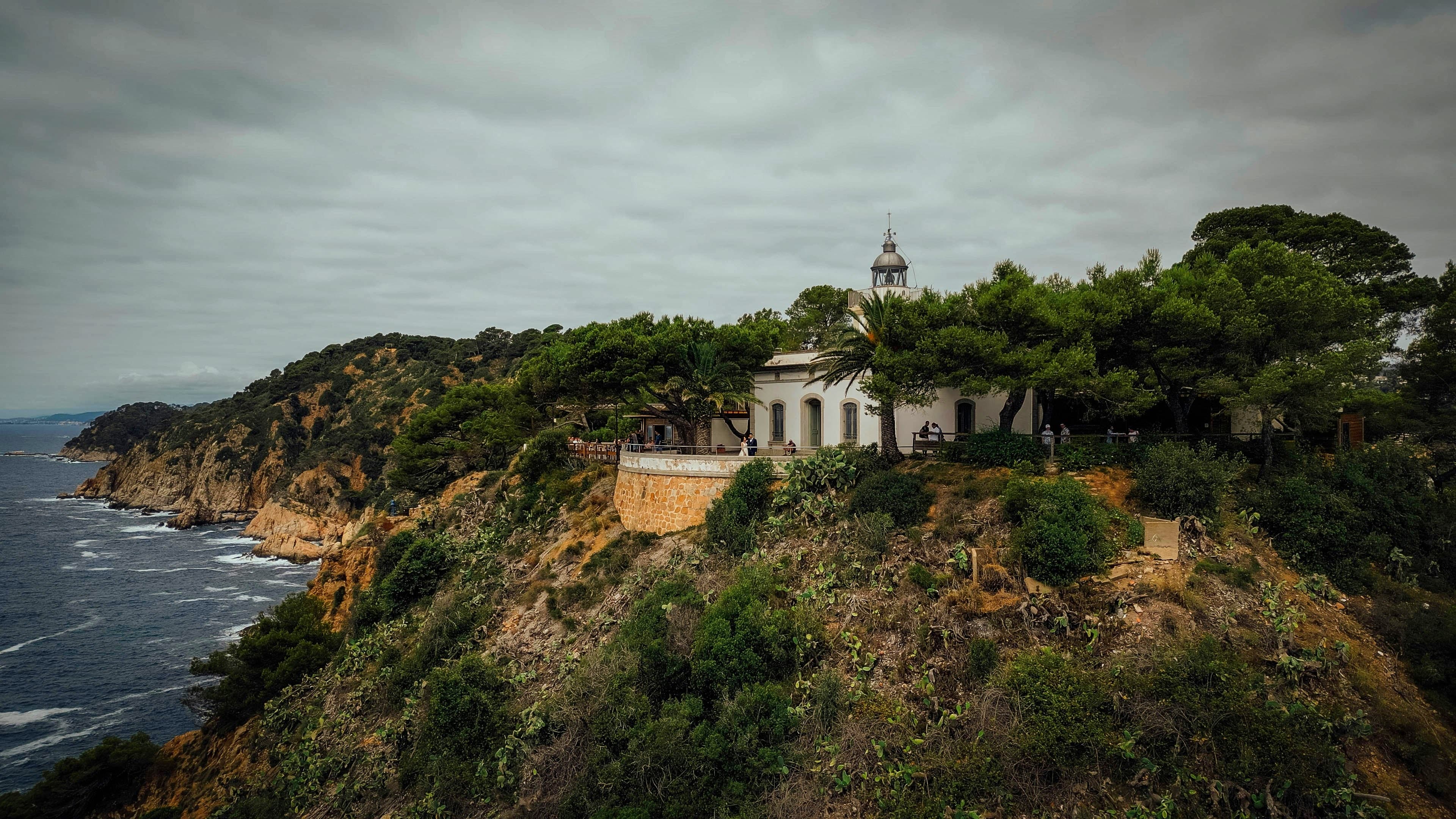 El faro de Tossa de Mar sobre el promontorio boscoso, entre pinos y acantilados, bajo un cielo encapotado